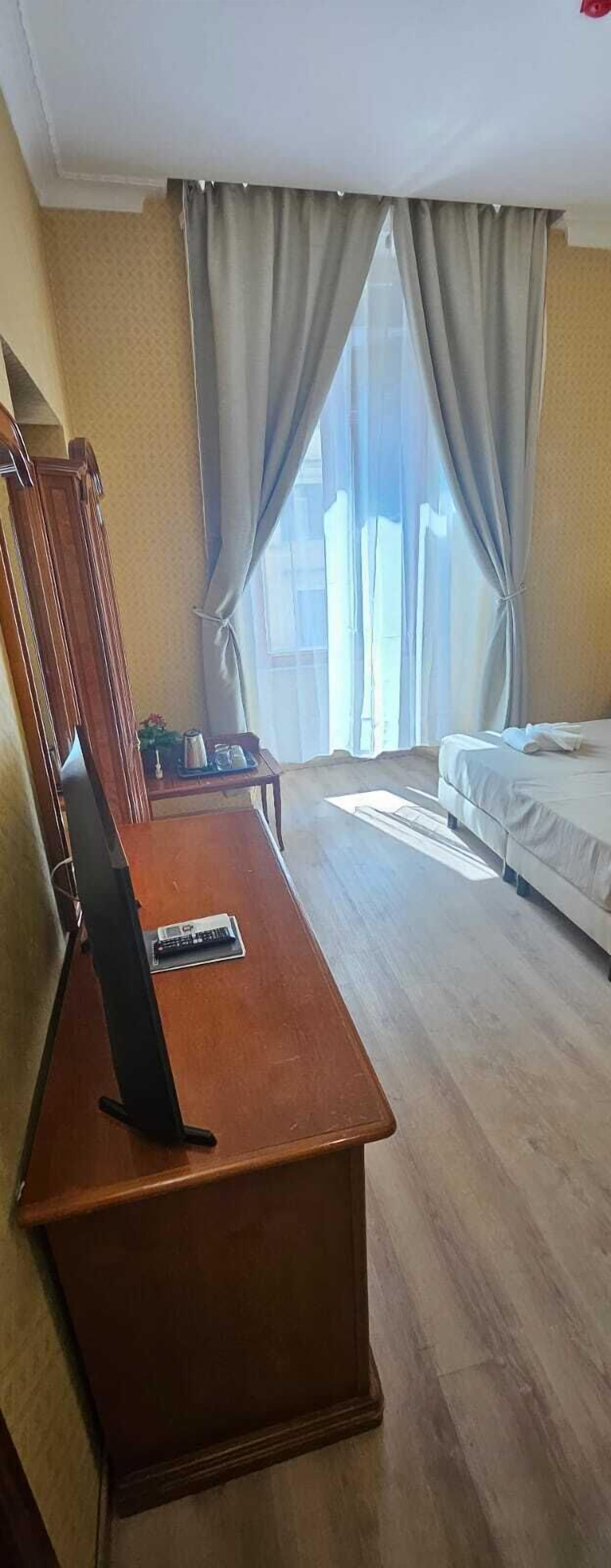 Ein Hotelzimmer mit einem hölzernen Schreibtisch, einem Bett und einem großen Fenster mit Vorhängen.