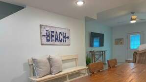 Un comedor con una mesa de madera y un banco, un televisor montado en la pared y un cartel que dice 