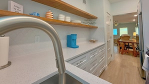 Una cocina moderna con un lavamanos de acero inoxidable, estantes de madera y armarios blancos.