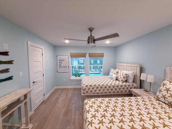 Une chambre avec deux lits, un ventilateur de plafond, une fenêtre avec des stores et une porte.