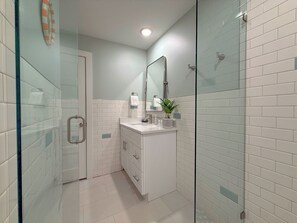 Une salle de bain moderne avec une douche à parois de verre, des murs recouverts de carreaux blancs et un meuble-lavabo blanc avec un miroir.
