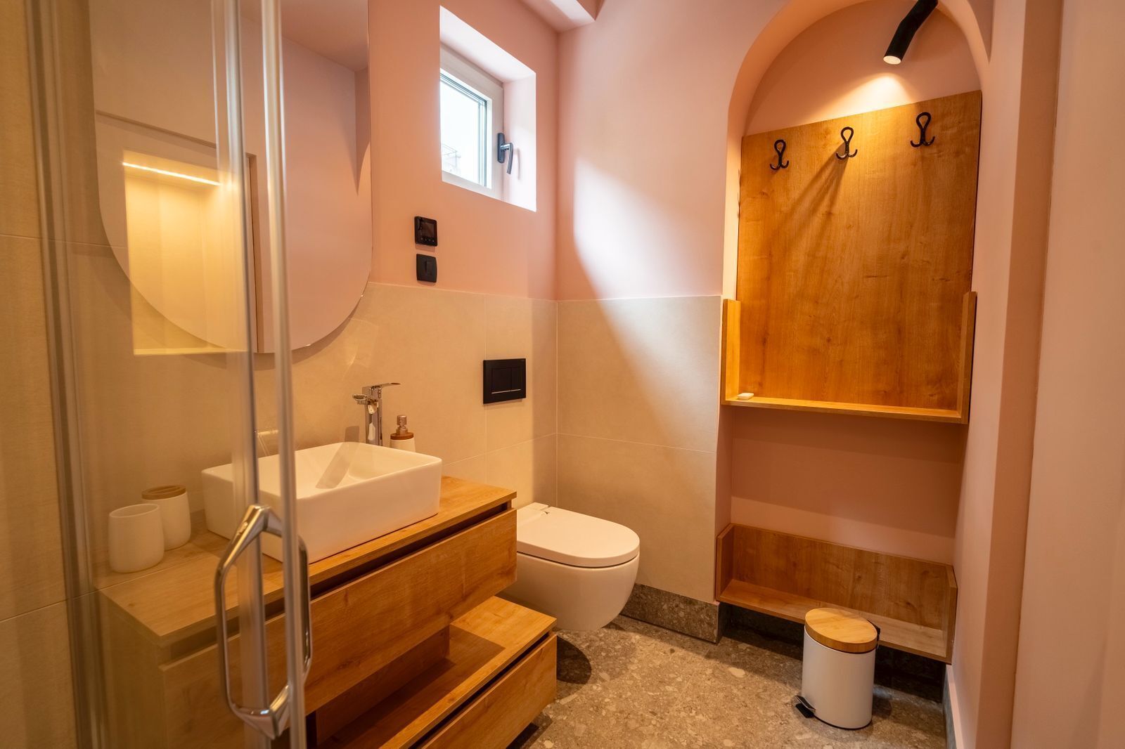 Un baño moderno con cabina de ducha de vidrio, lavamanos independiente, inodoro y mueble de tocador de madera con gabinete empotrado.