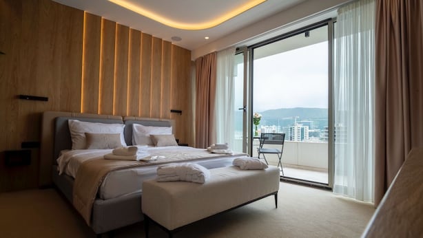 Una habitación de hotel moderna con una cama grande, un área de descanso y un balcón con vistas a la ciudad.