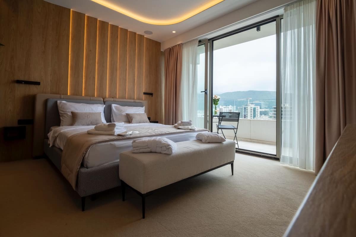 Una habitación de hotel moderna con una cama grande, un área de descanso y un balcón con vistas a la ciudad.