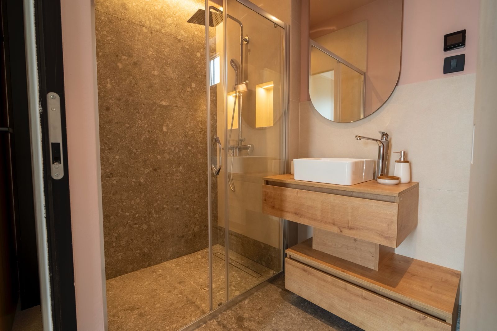 Une salle de bain moderne dotée d’une douche à parois de verre, d’un meuble-lavabo en bois et d’un miroir placé au-dessus du meuble-lavabo.
