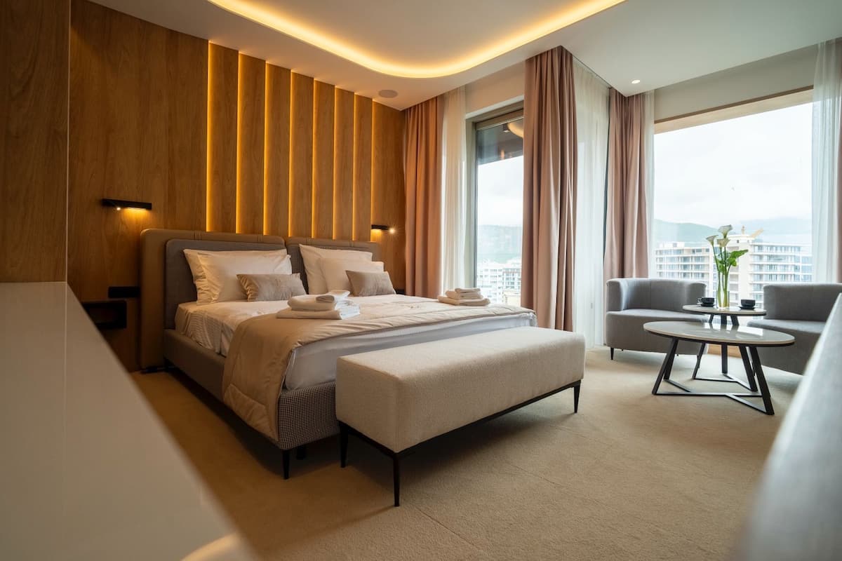 Una habitación de hotel moderna con una cama grande, un sofá, una mesita y vistas a la ciudad.