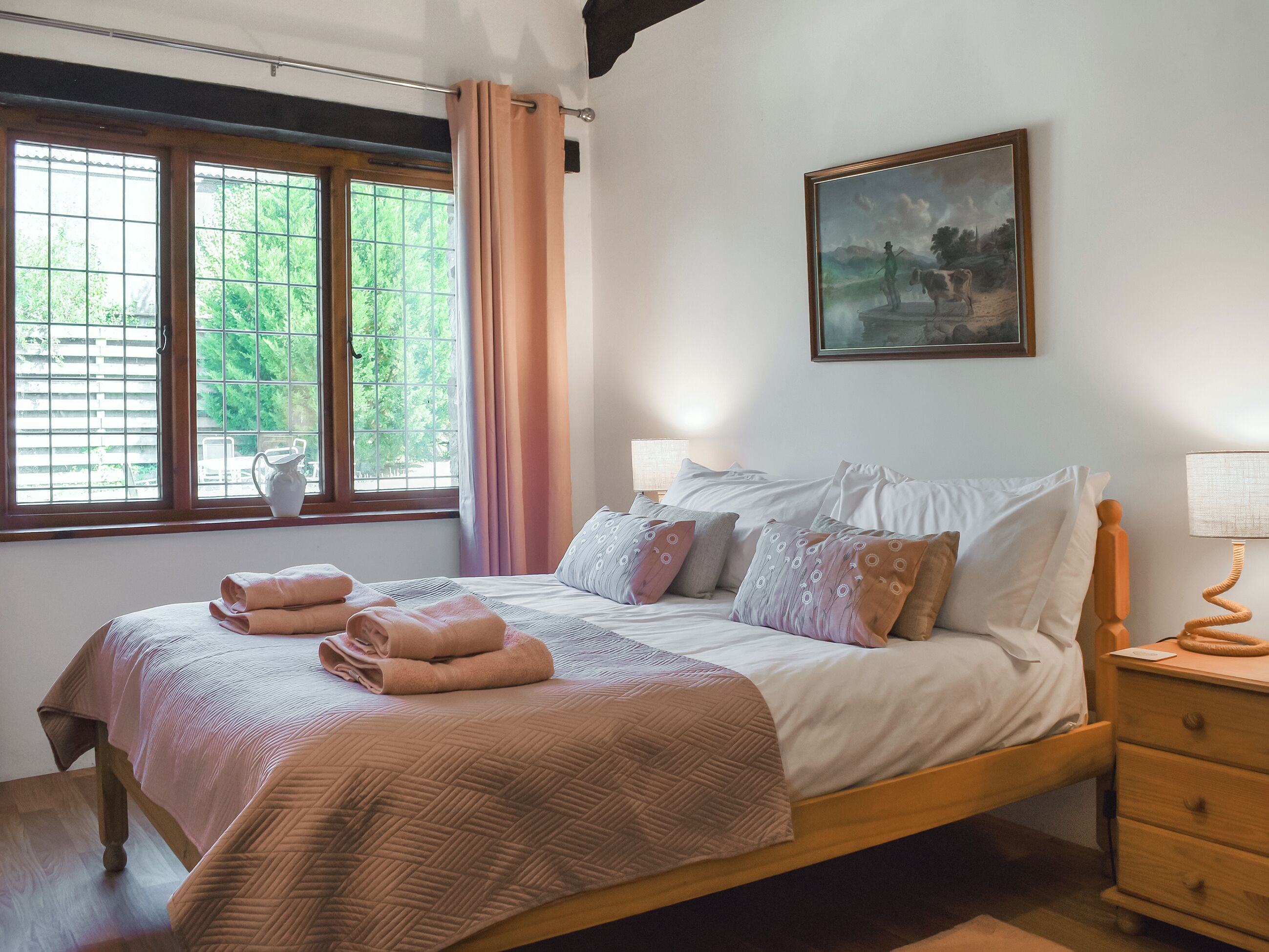 A bedroom with a bed, a painting, a window with curtains, and a bedside table.