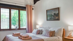 Een slaapkamer met een bed, een schilderij, een raam met gordijnen en een nachtkastje.