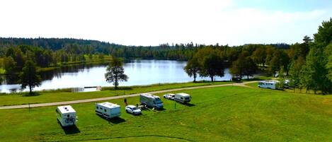 A campground with RVs parked on a grassy field near a lake, surrounded by trees.