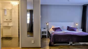 A modern hotel room with a large bed, bedside lamps, a mirror, and a bathroom with a sink and shower.