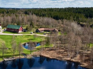 A rural landscape with a pond, a red barn, and a smaller building.