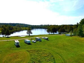 A campground with RVs parked on a grassy field, a lake in the background, and trees surrounding the area.