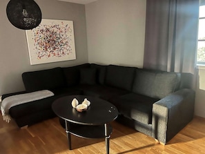 Un salon moderne avec un canapé noir, une petite table ronde et un tableau abstrait aux couleurs vives accroché au mur.