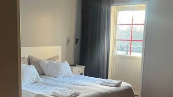 A hotel room with a bed, a nightstand, a lamp, a window with a view, and a curtain.