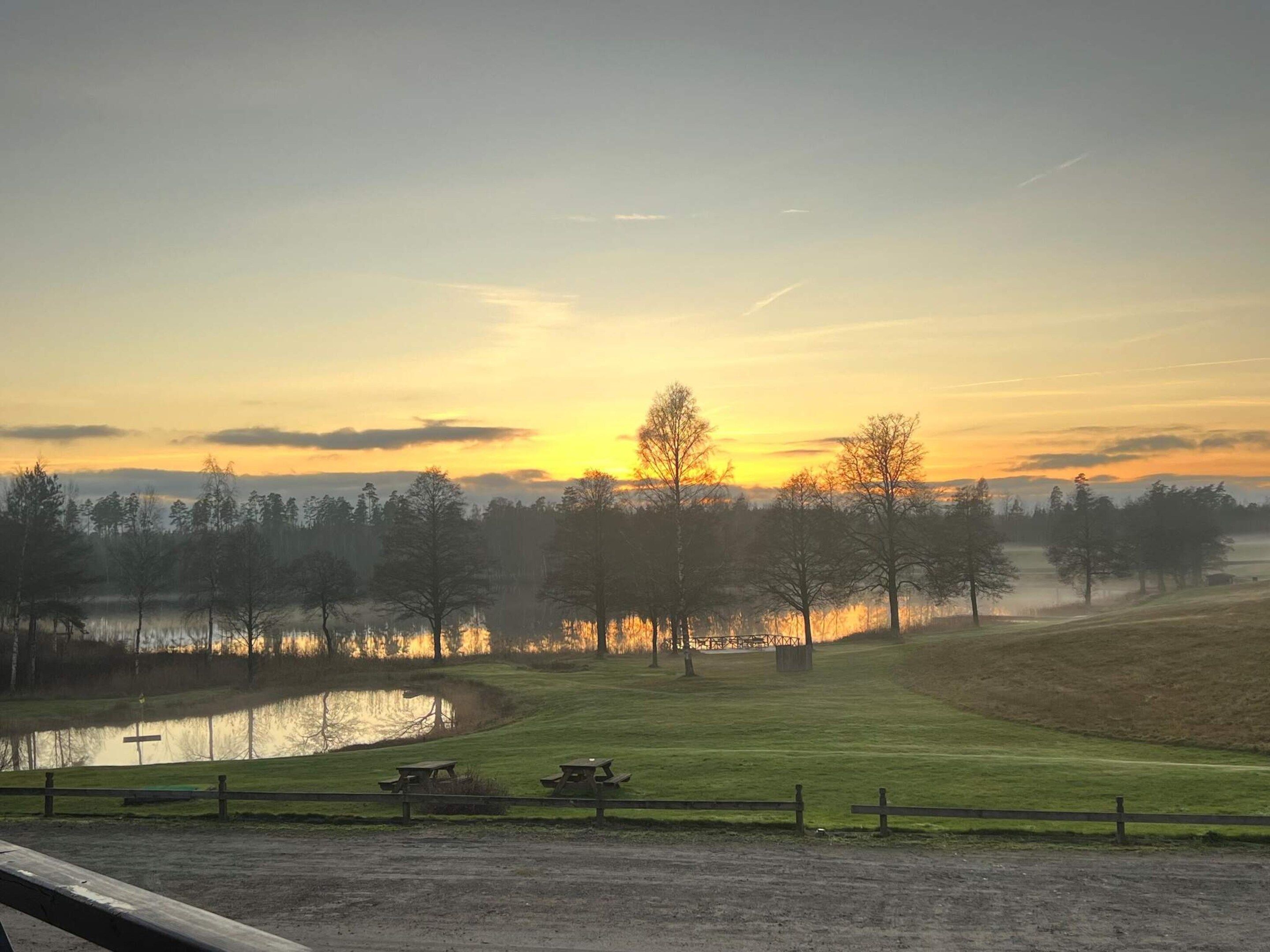 Panorama al tramonto su un prato erboso con un corso d'acqua e alberi.