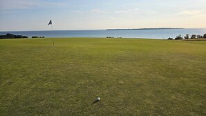 A golf course with a flagstick and a golf ball on the green, overlooking a body of water. - 5 Person Holiday Home in Stehag (Stehag)