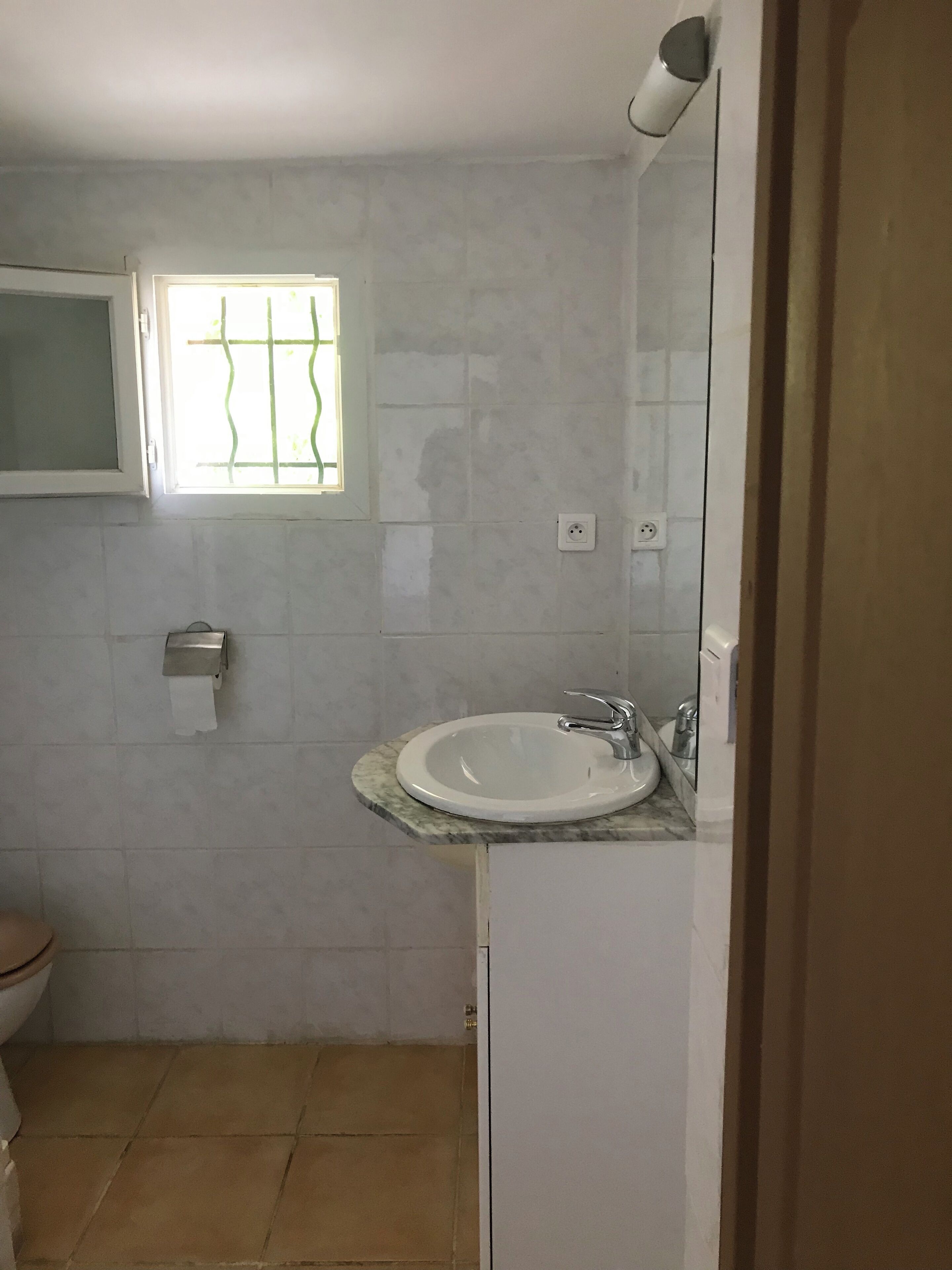 A bathroom with a toilet, a sink, a mirror, and a window with bars.