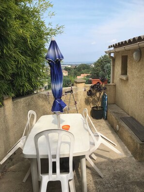 A patio with a white table and chairs, a blue umbrella, and a view of the city. - Location BORGO MARANA GOLO (Borgo)