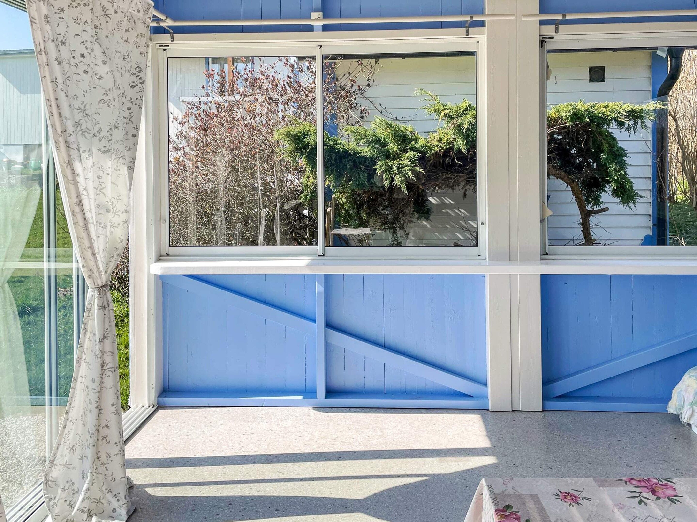 A room with a large window, a blue wall, and a view of trees and a house.