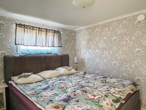 Un dormitorio con colcha estampada de flores, cabecera y ventana con cortinas traslúcidas.