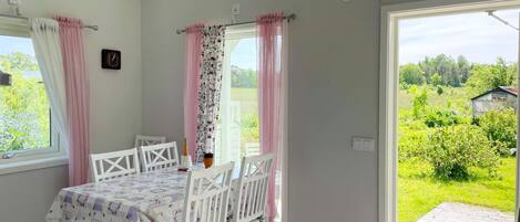 A room with a table and chairs, a clock on the wall, and a view of greenery outside.
