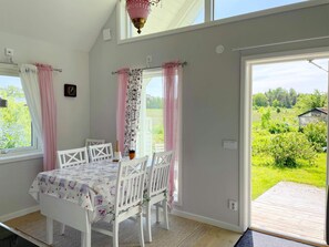 Une pièce avec une table et des chaises, une horloge au mur et une vue sur la verdure à l’extérieur.