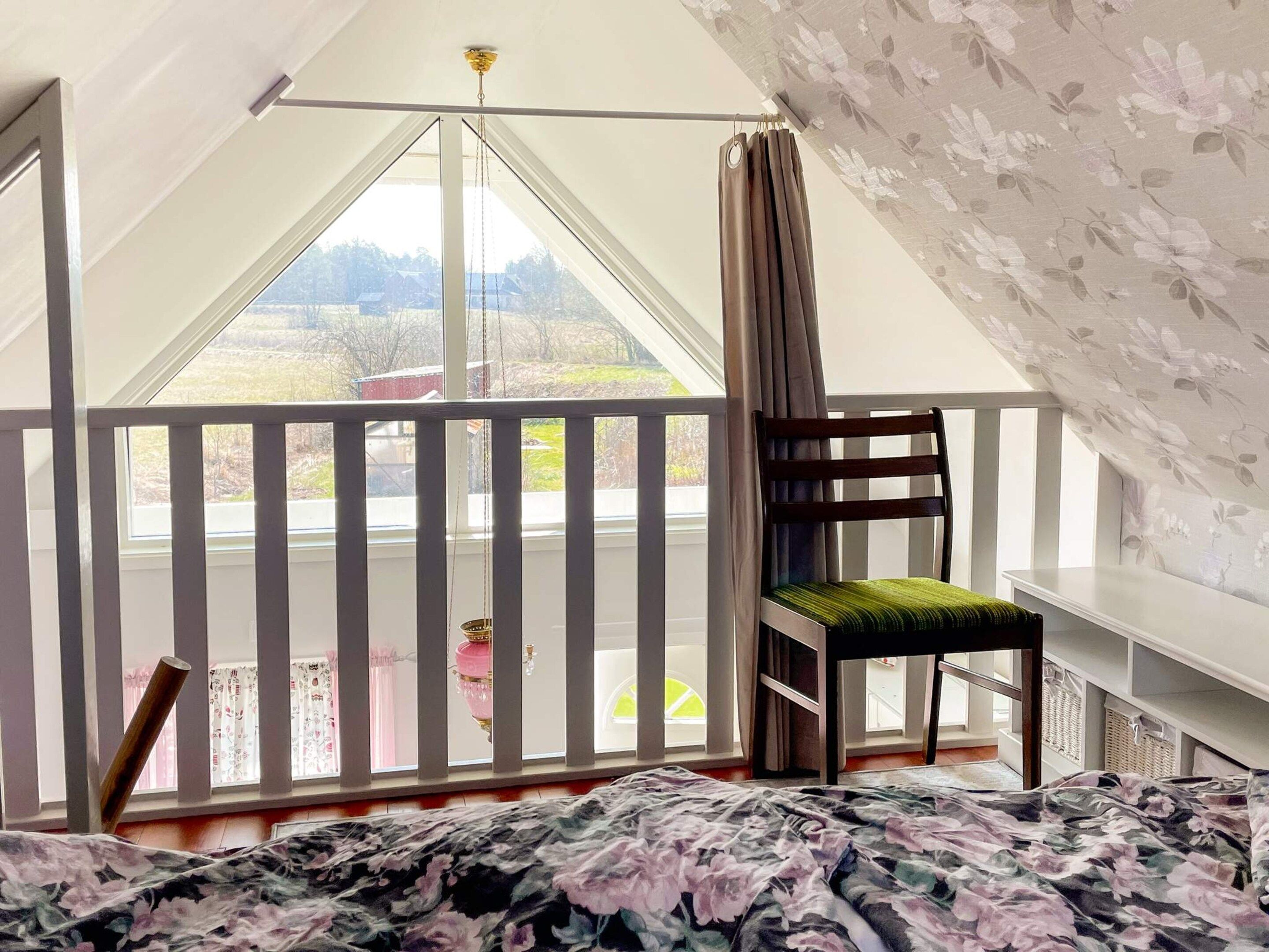 A bedroom with a bed, a chair, a window, and a balcony.
