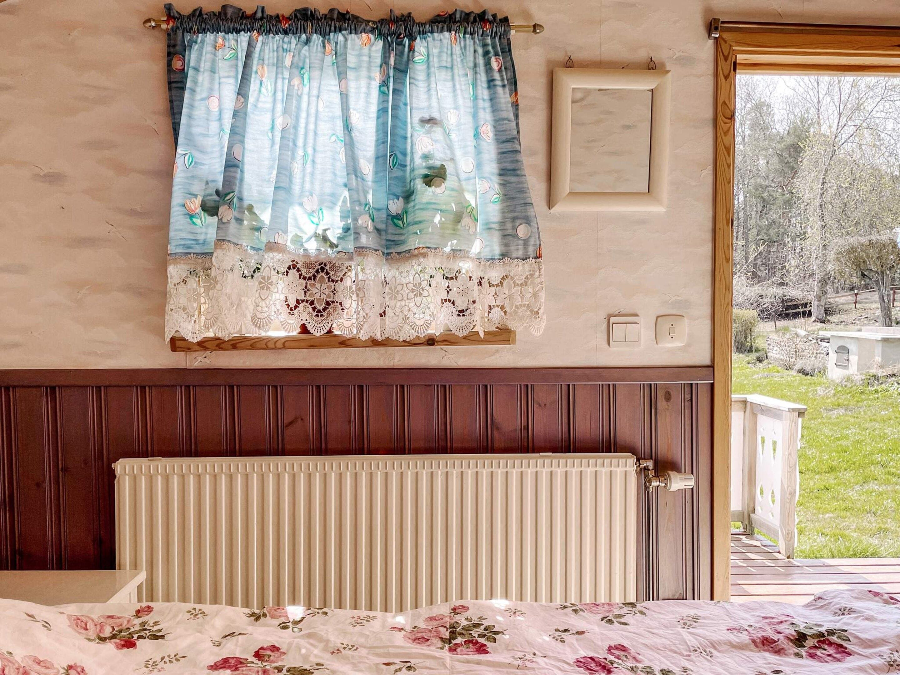 Een slaapkamer met een bed, een raam met gordijnen, een radiator en uitzicht op de omgeving.