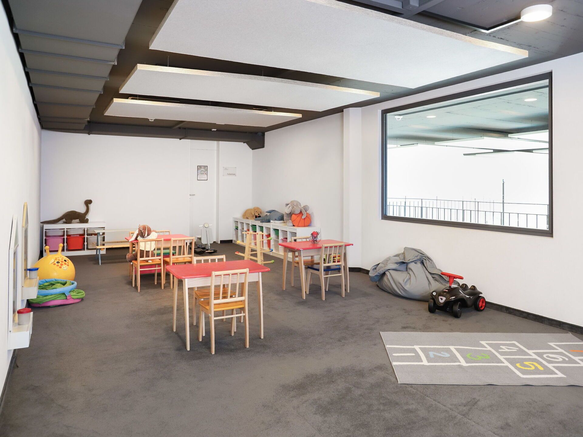 A classroom with tables and chairs, educational toys, and a large window with a view.
