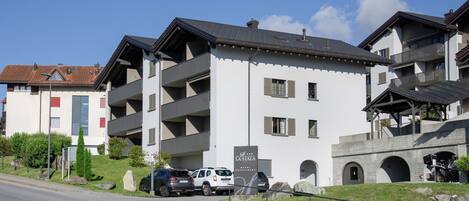 A multi-story hotel with balconies, a parking area, and a stone archway.