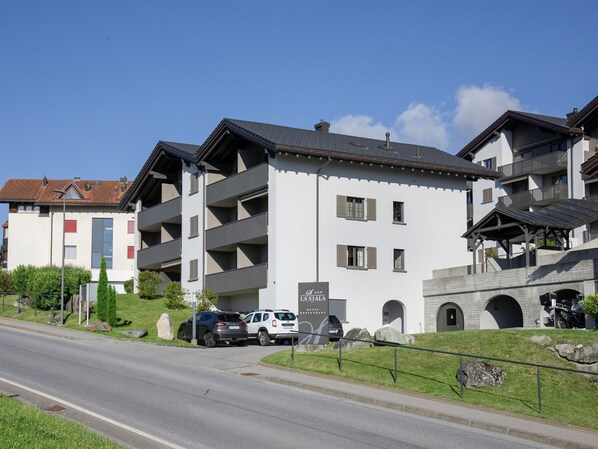 A multi-story hotel with balconies, a parking area, and a stone archway.
