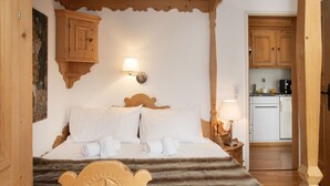 A wooden-framed bed with white linens and a decorative headboard, a wall-mounted lamp, and a view into a kitchen with wooden cabinets and a countertop. - Nice apartment for 2 guests with pool, WIFI, TV, patio, pets allowed and panoramic view (Falera)