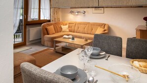 A cozy living room with a sofa, a dining table set with plates, glasses, and cutlery, and a window with curtains. - Lovely apartment for 3 people with pool, WIFI, TV, balcony and panoramic view (Falera)