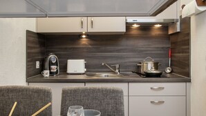 A compact kitchenette with a coffee maker, toaster, sink, and stove. There are two chairs and a table with glasses and a bowl. - Lovely apartment for 3 people with pool, WIFI, TV, balcony and panoramic view (Falera)