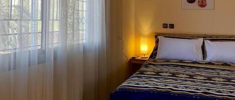 Ein Hotelzimmer mit Bett, Nachttisch, Lampe und einem Fenster mit Vorhängen.
