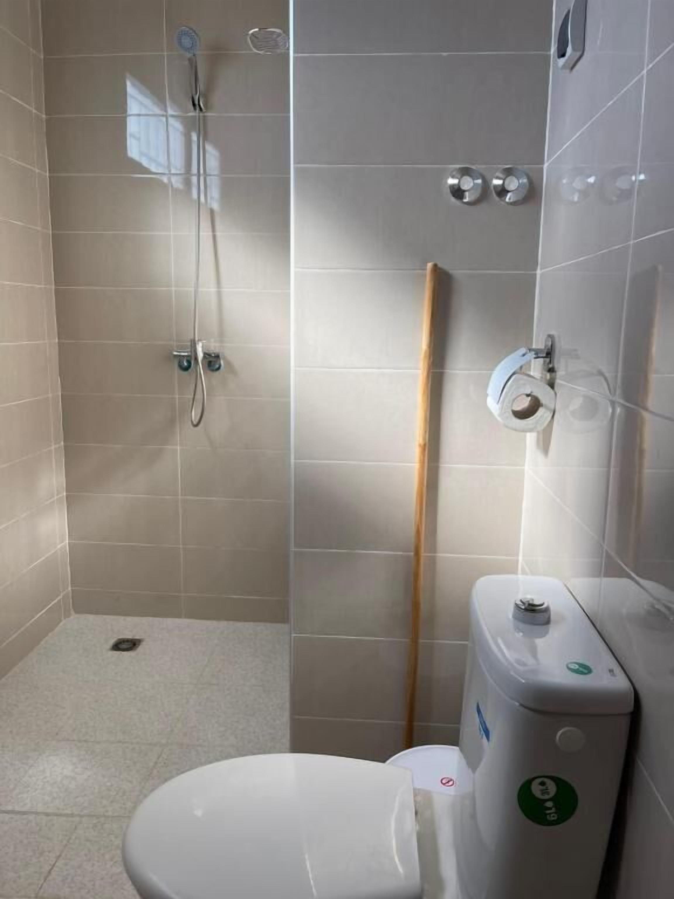 A small, tiled bathroom with a toilet, a shower, and a toilet paper holder.
