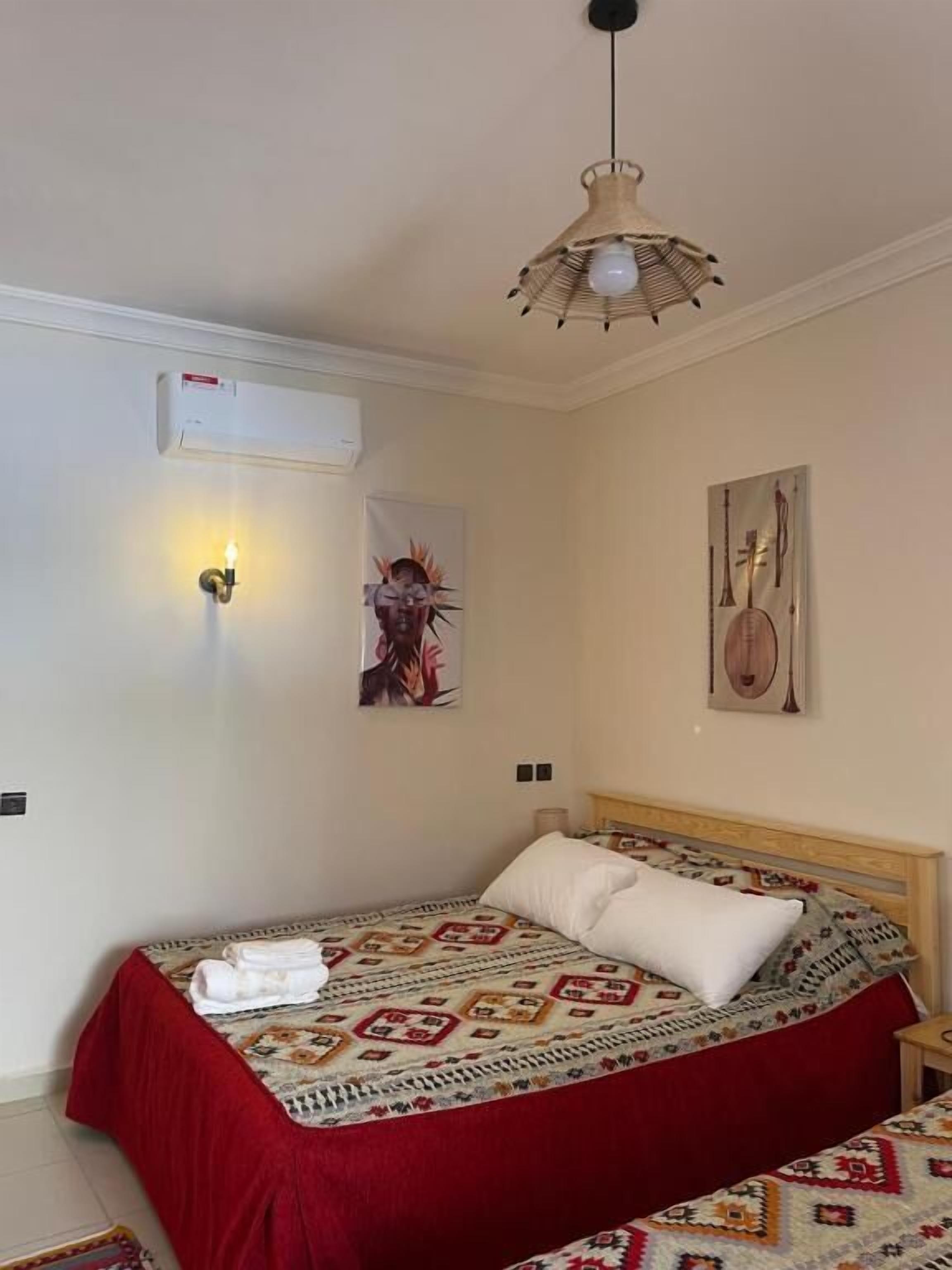 Un dormitorio con una cama, un aire acondicionado instalado en la pared, una lámpara fijada a la pared y un cuadro de instrumentos musicales.