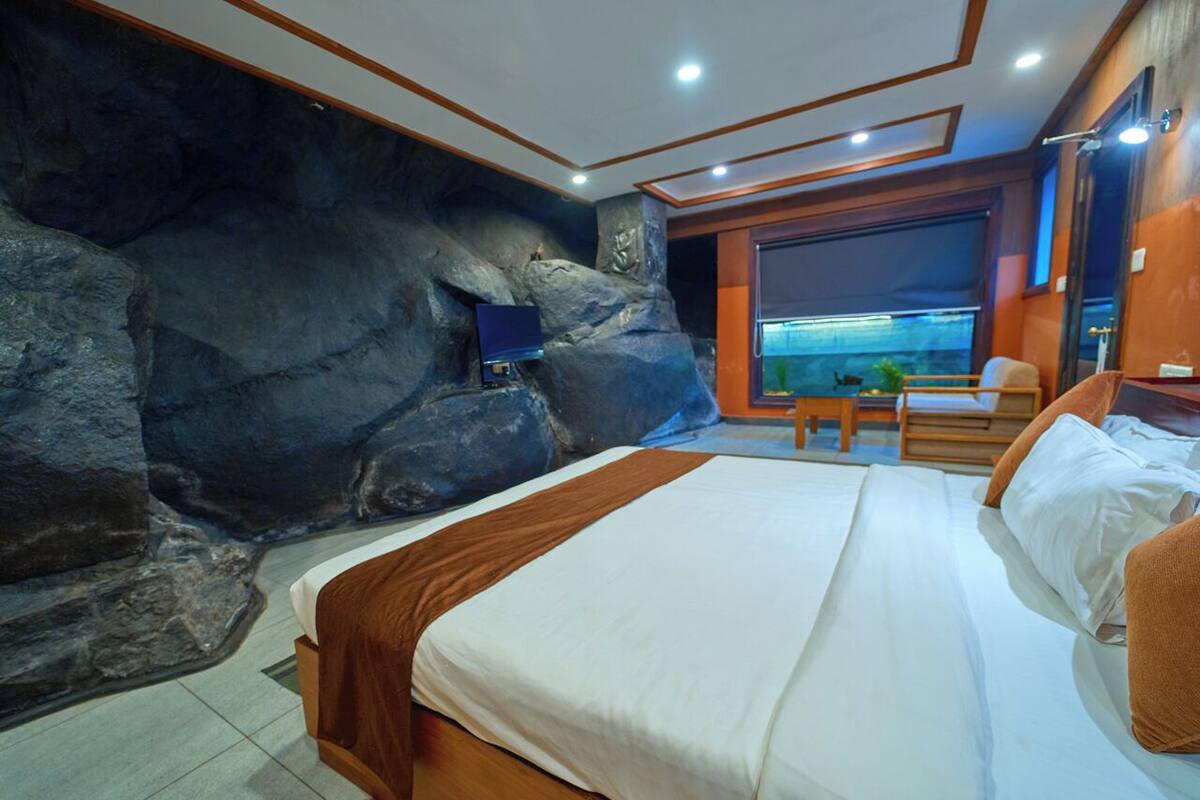 Une chambre avec un grand lit, une vue sur la mer par la fenêtre et un mur en pierre.