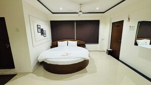 A bedroom with a round bed, a ceiling fan, and a large window with dark curtains. - Hotel Palladium (Surat)