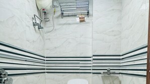 A small bathroom with a toilet, a sink, a shower, and a blue basin. - Hotel Palladium (Surat)