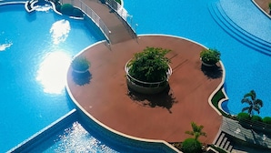Uma grande piscina circular com uma ilha central, rodeada por um passeio e palmeiras.