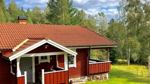Une maison en bois rouge avec un toit en tuiles, une véranda et un petit abri attenant.