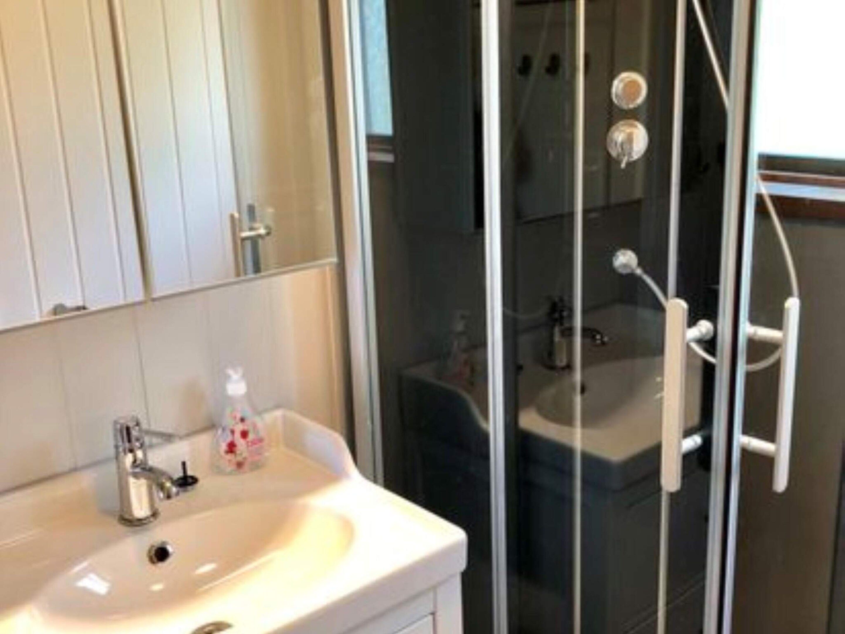 Un baño con un lavamanos blanco, una cabina de ducha de vidrio y un espejo sobre el lavamanos.