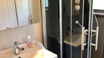 Un baño con un lavamanos blanco, una cabina de ducha de vidrio y un espejo sobre el lavamanos.