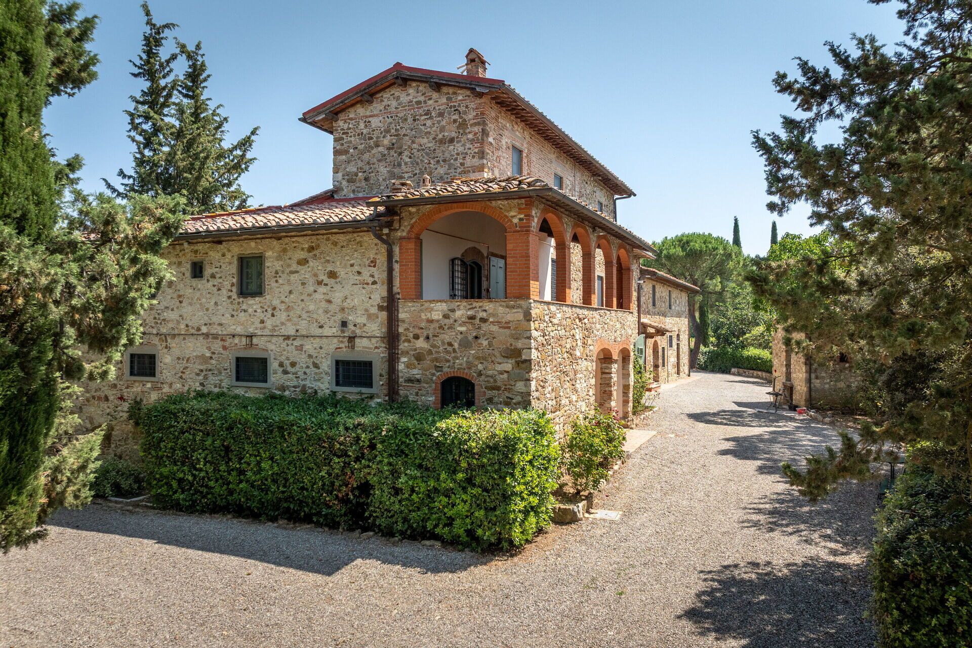A stone building with a tiled roof, arched windows, and a gravel driveway.