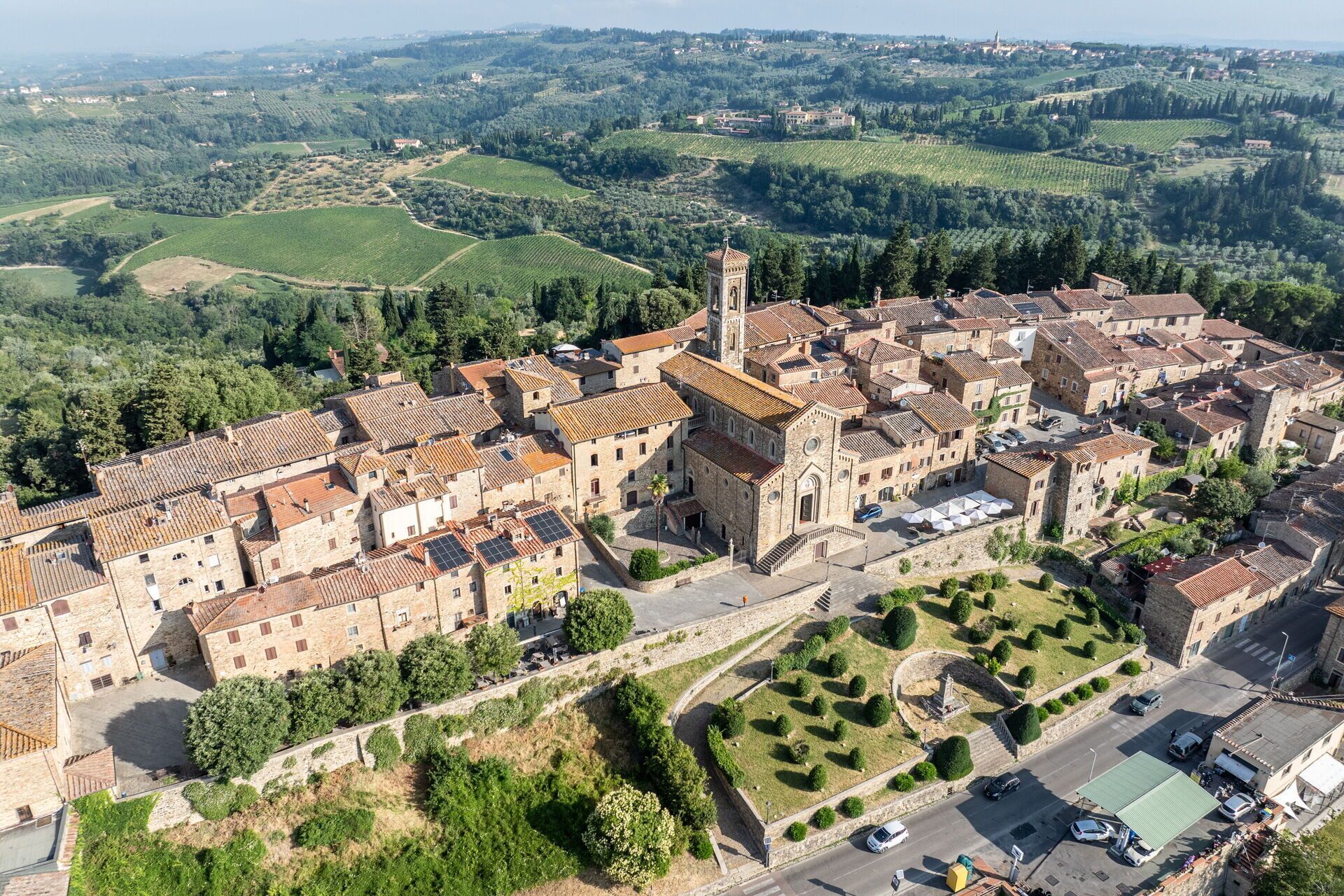 An aerial view of a historic town with stone buildings, a central church, and surrounding vineyards.