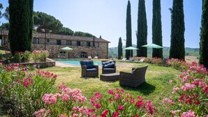 A stone villa with a swimming pool, surrounded by tall cypress trees and vibrant pink flowers. - Cosy apartment in villa for 4 people with pool, WIFI and TV, close to Greve In Chianti (Badia A Passignano)