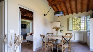 A cozy dining area with a round table and six chairs, a wooden ceiling, and a window with a view of trees. - Nice apartment in villa with WIFI, pool, patio and panoramic view, close to Greve In Chianti (Badia A Passignano)