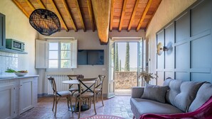 Una cocina acogedora con vigas de madera, un comedor con mesa y sillas, y un sofá gris con una manta roja.