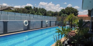 Une piscine dont le bord est recouvert de carreaux bleus, entourée d’un mur gris sur lequel sont fixées deux bouées de sauvetage.